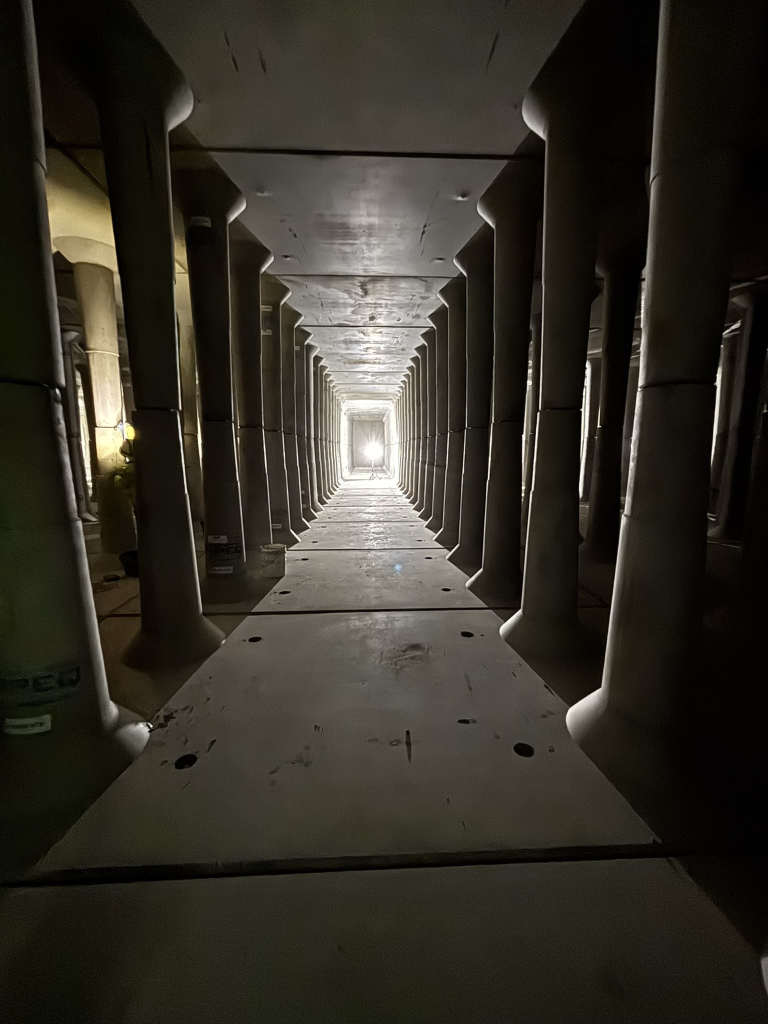 A long hallway with pillars and a light coming from the center.